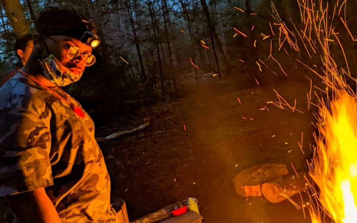 a student stands beside a campfire on a backpacking and rock climbing trip with outward bound